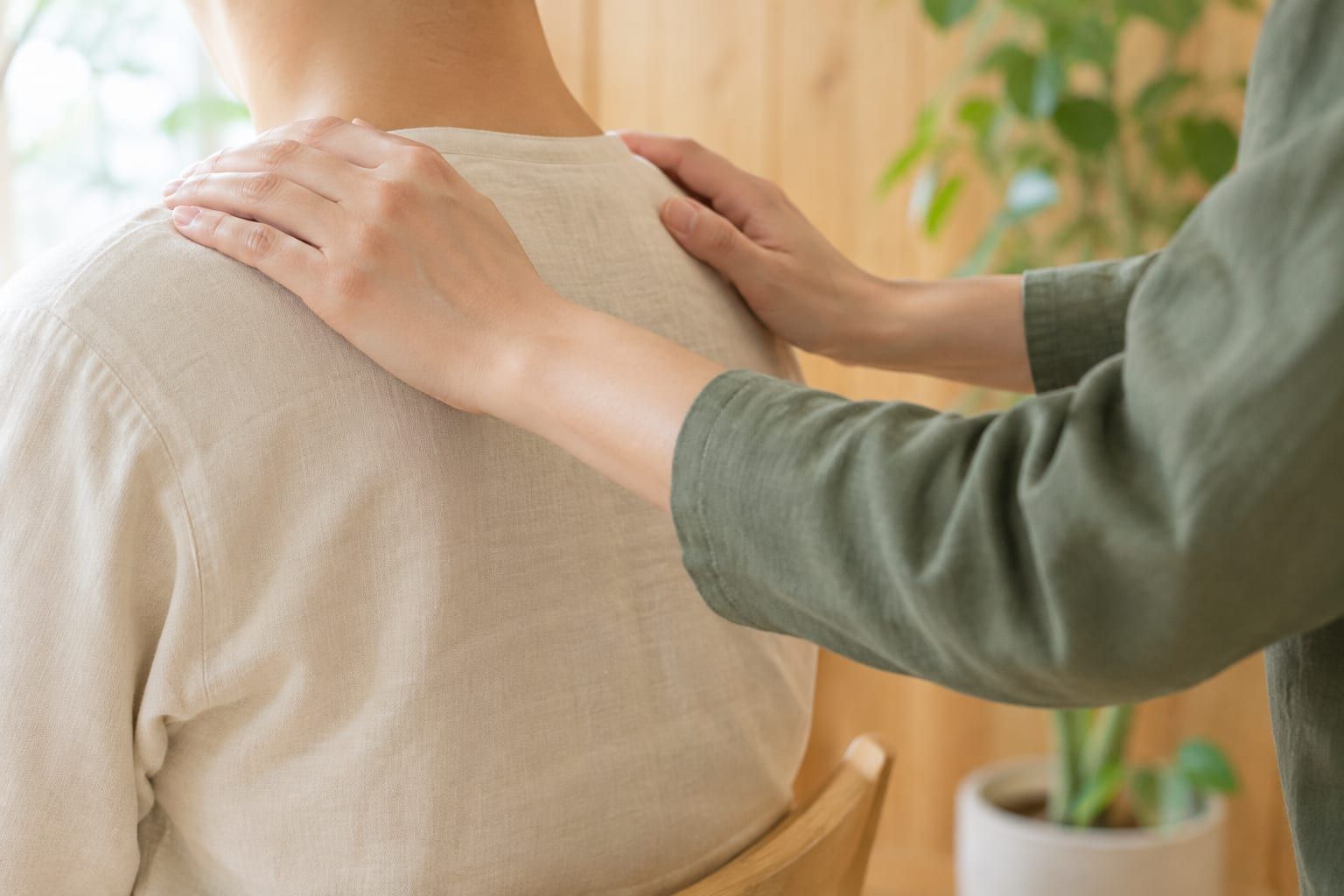 いすに座った人の肩に、施術者の両手がそっと添えられている